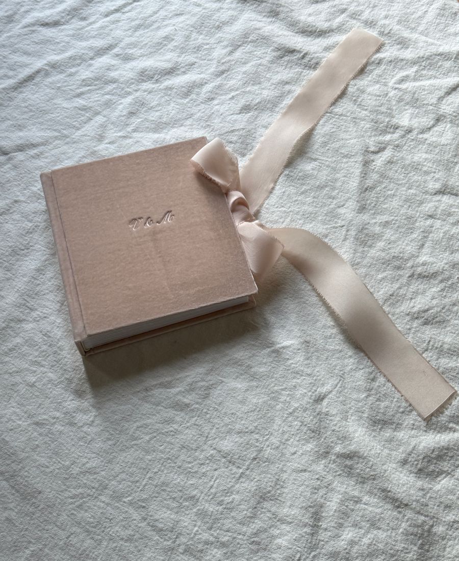A linen-bound photo album with a ribbon closure and embossed initials